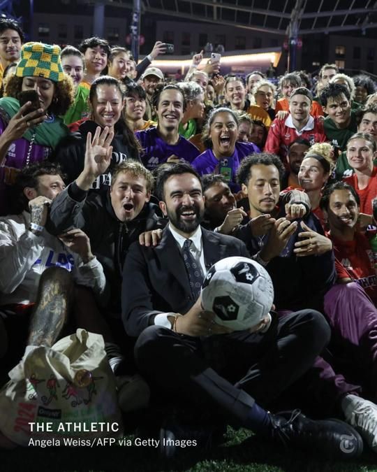 Zohran Mamdani poses holding a soccer ball with a bunch of excited players.