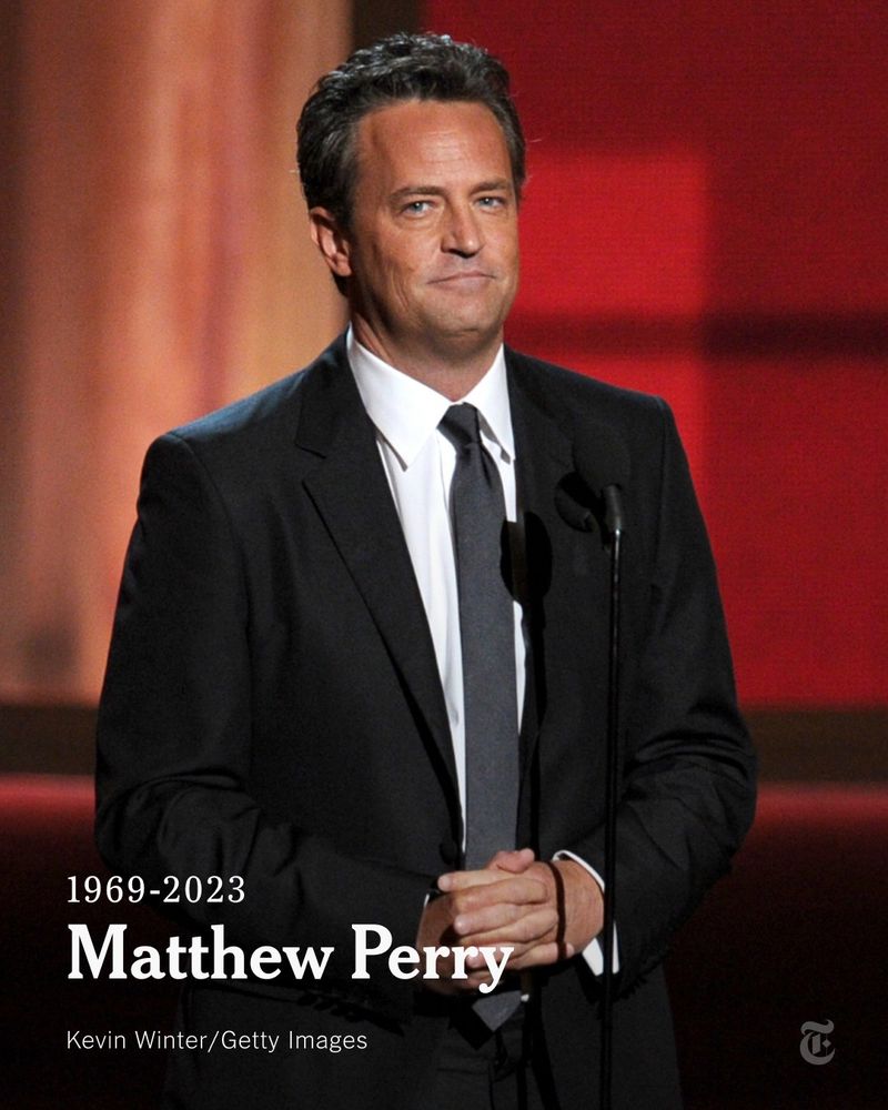 Matthew Perry is standing onstage behind a microphone at the 64th Annual Primetime Emmy Awards in 2012. He is wearing a black suit, a white shirt and a black tie. A headline reads: "1969-2023: Matthew Perry." Photo by Kevin Winter/Getty Images.