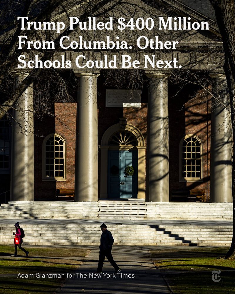 Two people walk through the dappled light of a courtyard in front of a brick building with a columned entrance, flanked on both sides by tall trees, on Harvard University’s campus. A headline reads: "Trump Pulled $400 Million From Columbia. Other Schools Could Be Next." Photo by Adam Glanzman for The New York Times