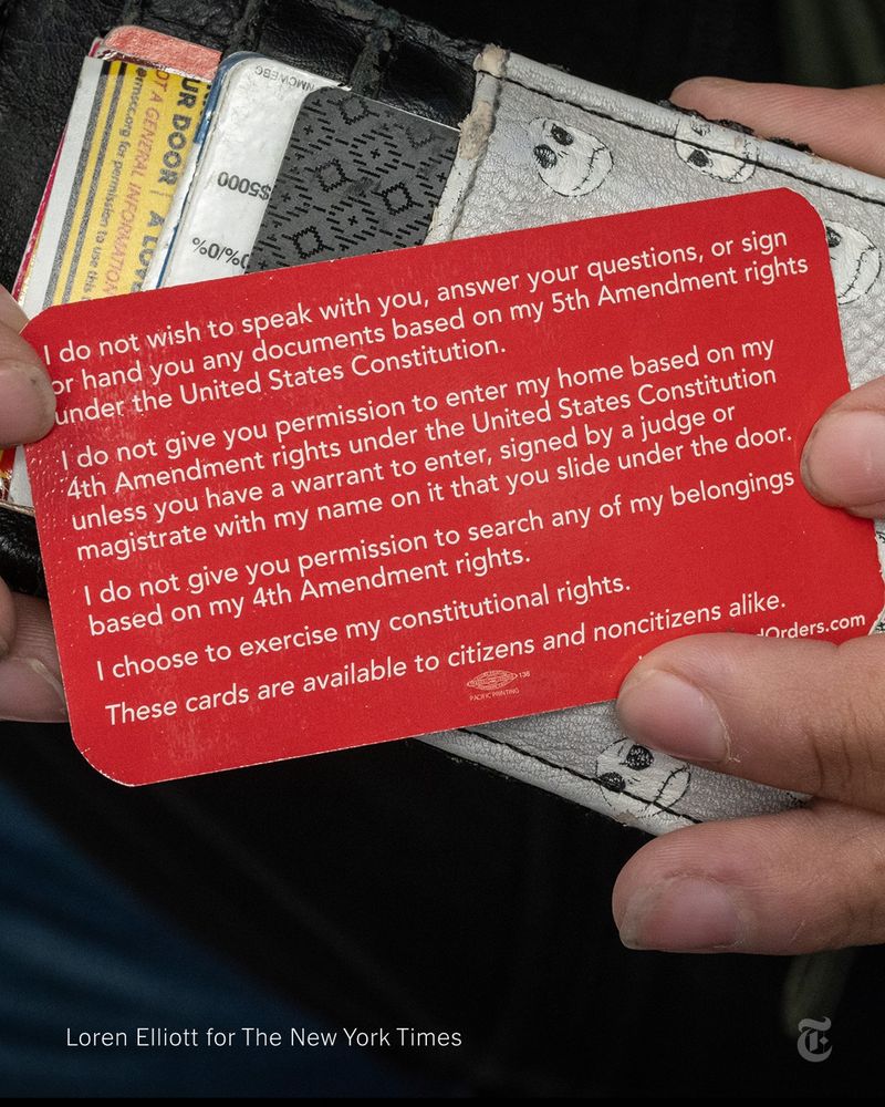 Two hands hold a small red card with white lettering against a wallet. The card reads:  “I do not wish to speak with you, answer your questions, or sign or hand you any documents based on my 5th Amendment rights under the United States Constitution. I do not give you permission to enter my home based on my 4th Amendment rights under the United States Constitution unless you have a warrant to enter, signed by a judge or magistrate with my name on it that you slide under the door. I do not give you permission to search any of my belongings based on my 4th Amendment rights. I choose to exercise my constitutional rights.” Photo by Loren Elliott for The New York Times.
