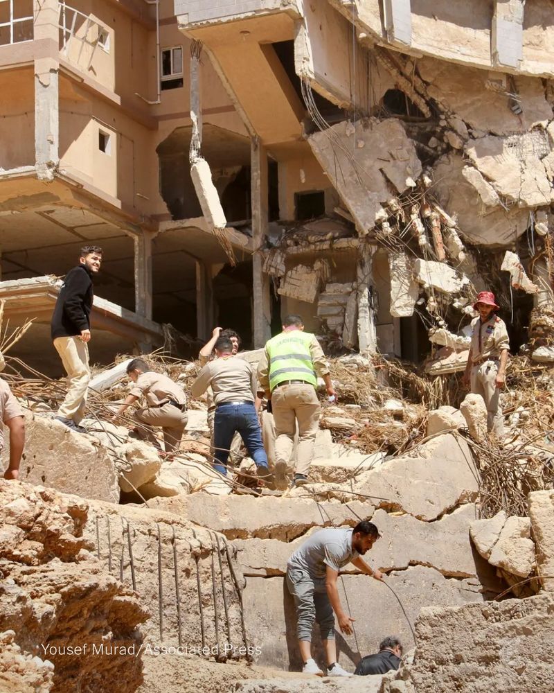 People, some in hard hats or safety vests, look for survivors in Derna, Libya. Photo by Yousef Murad/Associated Press.