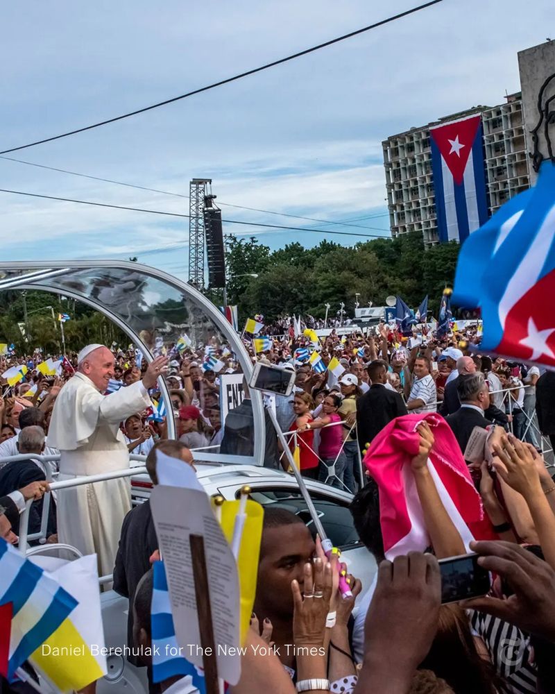 Pope Francis waves to a large crowd of people, some of whom are waving Cuban flags or holding up their phones to take photos. Photo credit: Daniel Berehulak for The New York Times