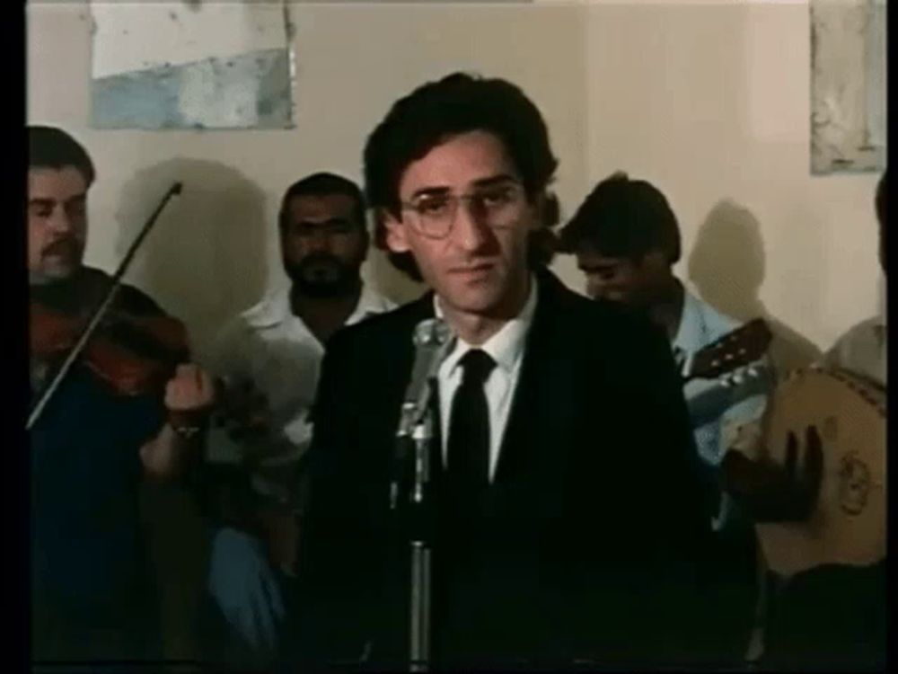 a man in a suit and tie is standing in front of a microphone in front of a band .