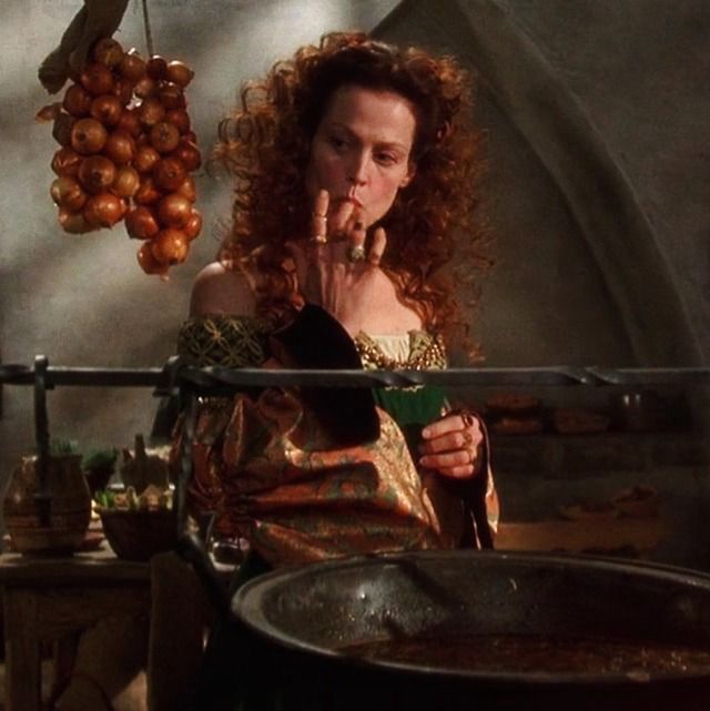 sigourney weaver sucking on her middle finger in a medieval fantasy kitchen standing by a big cauldron, onions are hanging next to her 