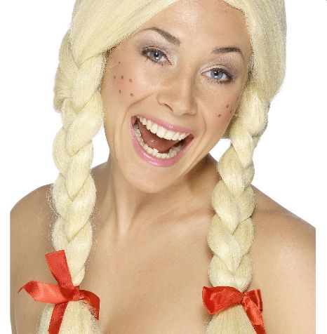 a white woman modelling a blonde wig in braids on either side of her head, tied at the bottom with red ribbon bows. she has large freckles drawn on her cheeks and is smiling painfully