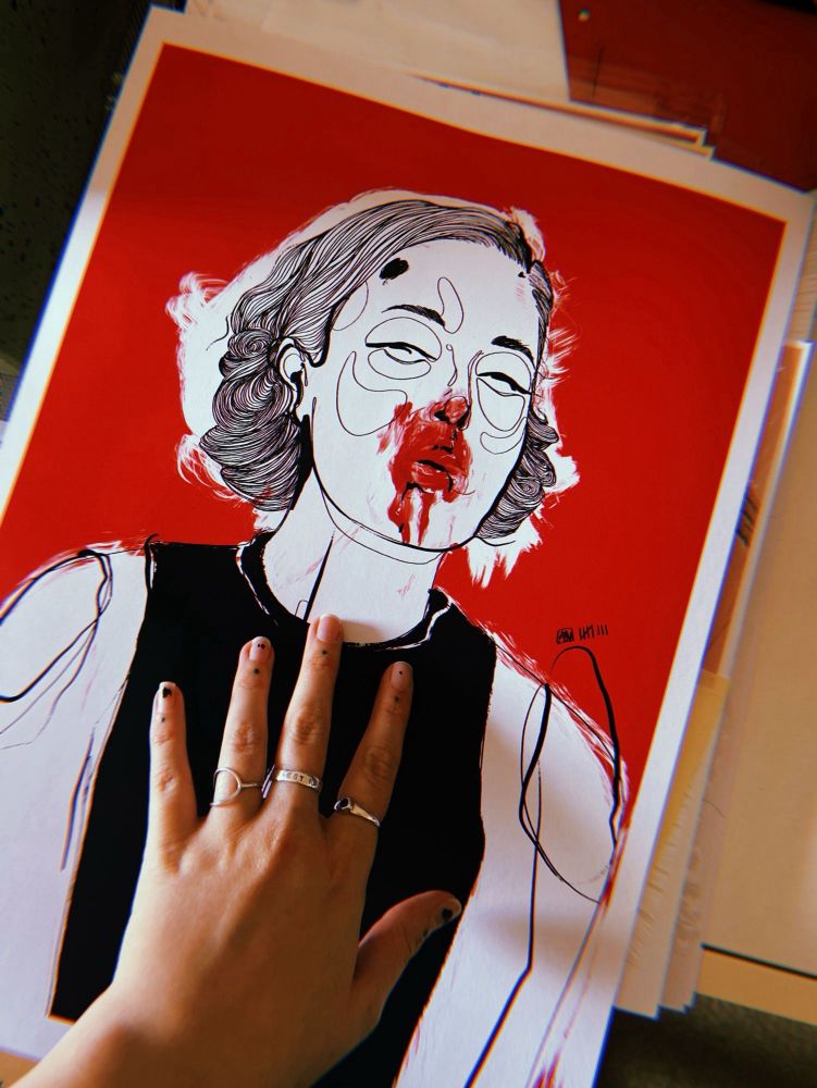 ni’s hand wearing three rings on her fingers, touching a drawing of phoebe waller-bridge (fleabag). a woman with short curly hair wearing a black jumpsuit. she has a bloody nose and mouth. the background is red.