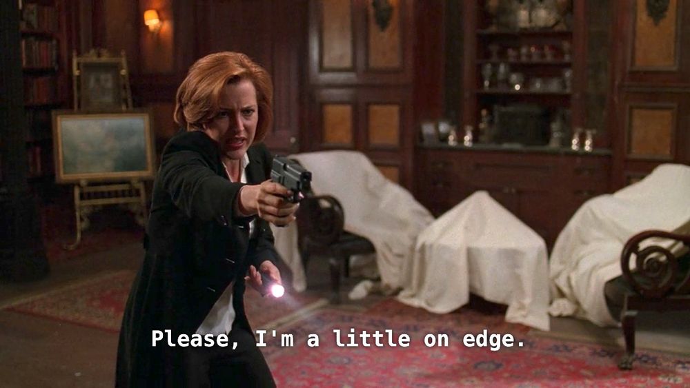dana scully (a white woman in a suit with short red hair) holding a gun and a torch, captions read “please, i’m a little on edge”. she is in a room adorned with furniture covered in white sheets.