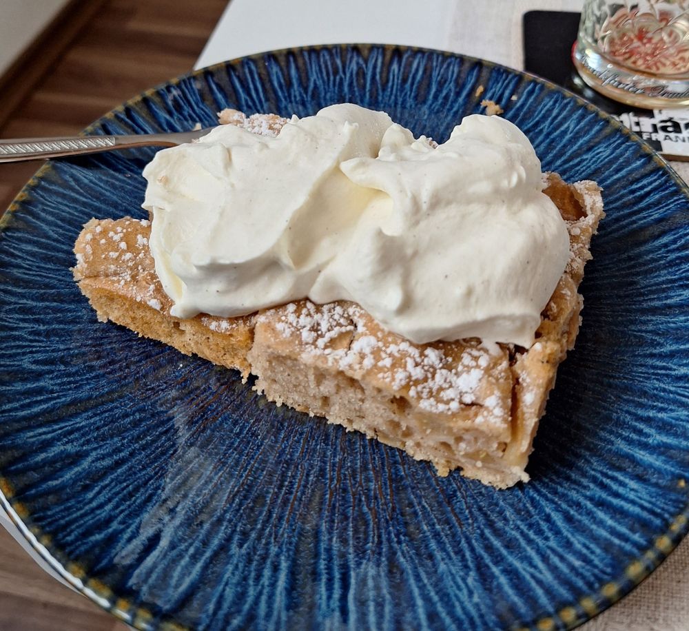 Stück Apfelkuchen mit Sahne obendrauf auf einem blauen Desserteller. 