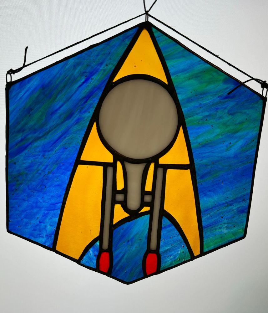 Stained glass of the starship Enterprise from Star Trek overlaying the federation insignia in a hexagon.