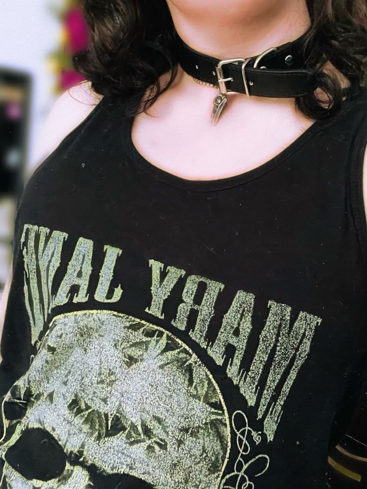 A photo of my chest, I am wearing a black tank top with a green skull and text that reads “MARY JANE”. I am wearing a black collar and have wavy black hair.