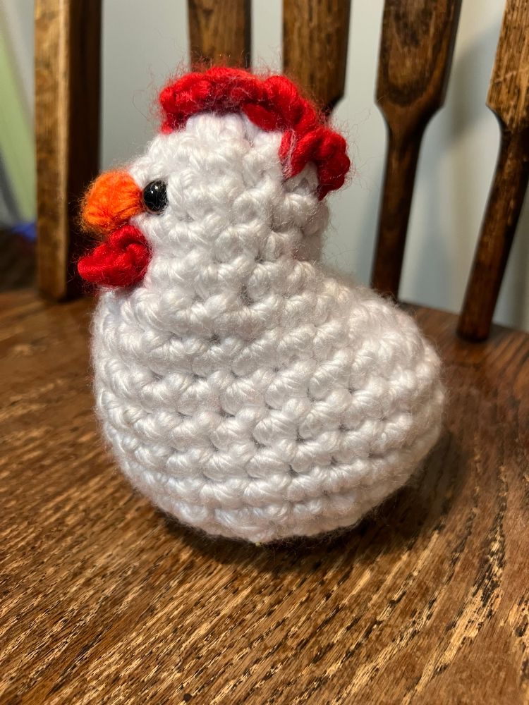Photo of crochet white chicken with red comb, yellow beak, and red woddles, one photo of chicken facing sideways.