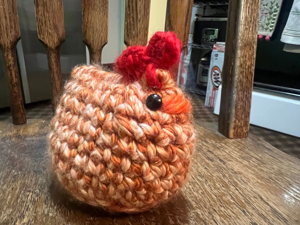 Orange and white stuffed crochet chicken from side.
