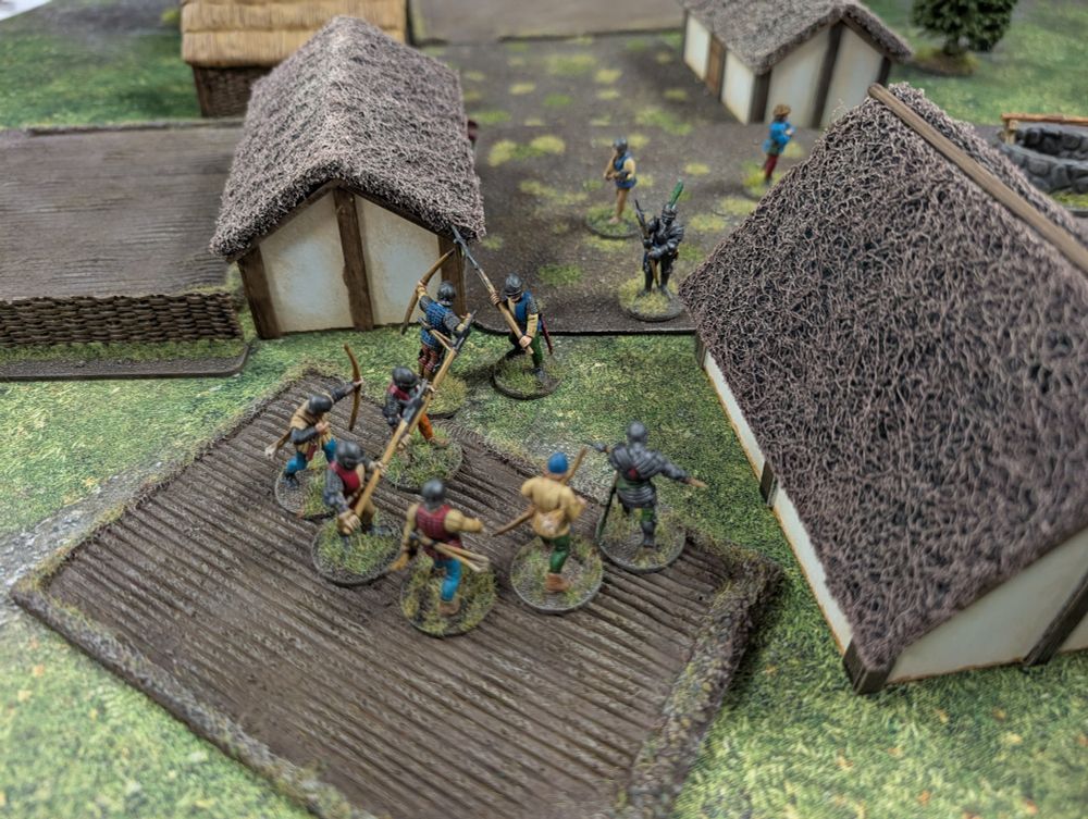 Various 28mm Wars of the Roses figures, positioned mid-game. Between two medieval buildings.