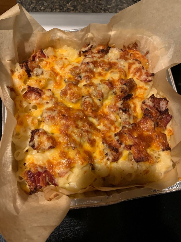 picture of an oh so delectable pan of baked, bacon crusted mac and cheese. underneath the beautiful golden crust of cheese is a blend of cheddars—yellow and white—swiss, gruyere and gouda married with white rice noodles and a touch of garlic.