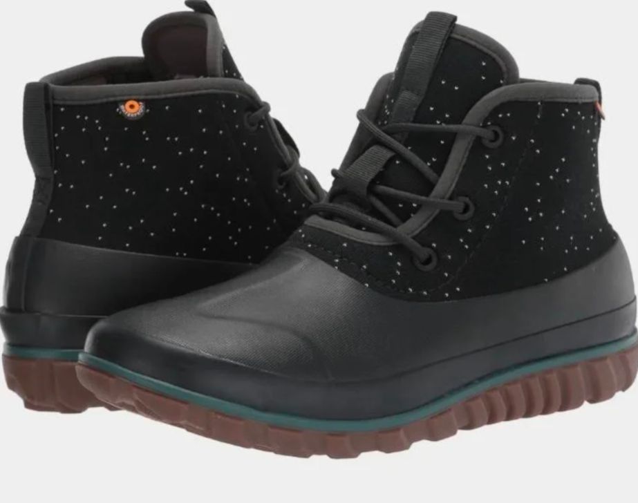 Bogs website photo. Forest green short ankle boots. The bottom foot area is solid green rubber with brown sole, and the upper is a green neoprene fabric with white speckles. The upper laces up with three eyelets.
