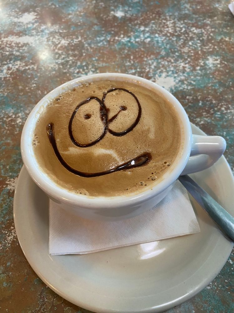 Latte art with a goofy, somewhat confused face with an off-to-the-side smile.