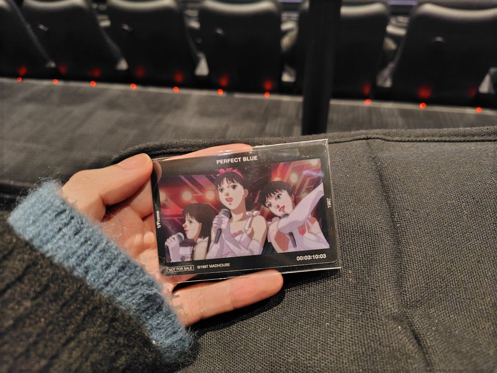 PERFECT BLUEの劇中画が使用されているカードを手に持っている画像。カードにはマイクを握った人間3名が描かれている。