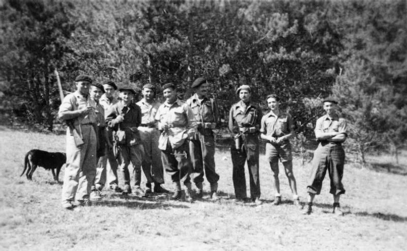 Krystyna Skarbek, second from right, with a group of male maquis fighters. The maquis are wearing combat gear and berets. 

