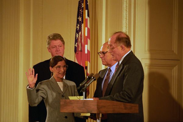 Ruth Bader Ginsberg being sworn in, with Bill Clinton behind her. She is short, and had yet to develop her signature giant collar style.