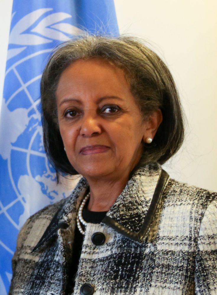 Sahle-Work Zewde standing in front of a UN flag. She is a Black woman with dark hair that is turning silver at the temples.