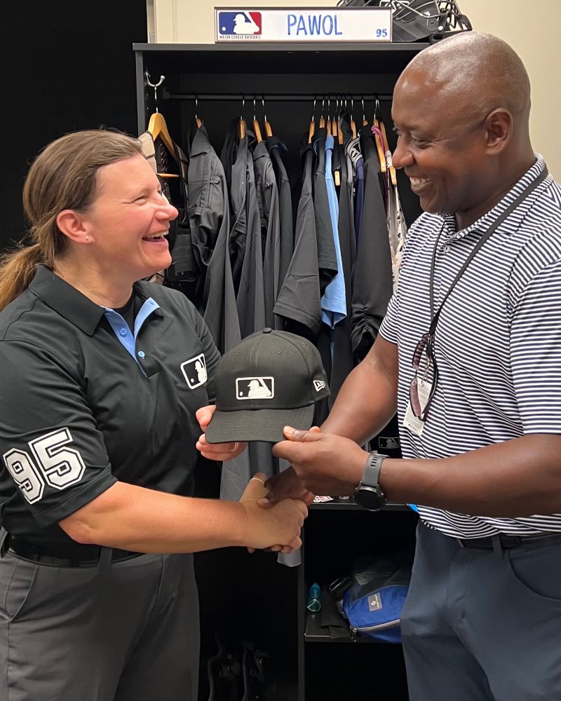 Jen Pawol, left, stands at her locker and shakes hands with Michael Hill, Major League Baseball Senior Vice President of On-Field Operations and Workforce Development.