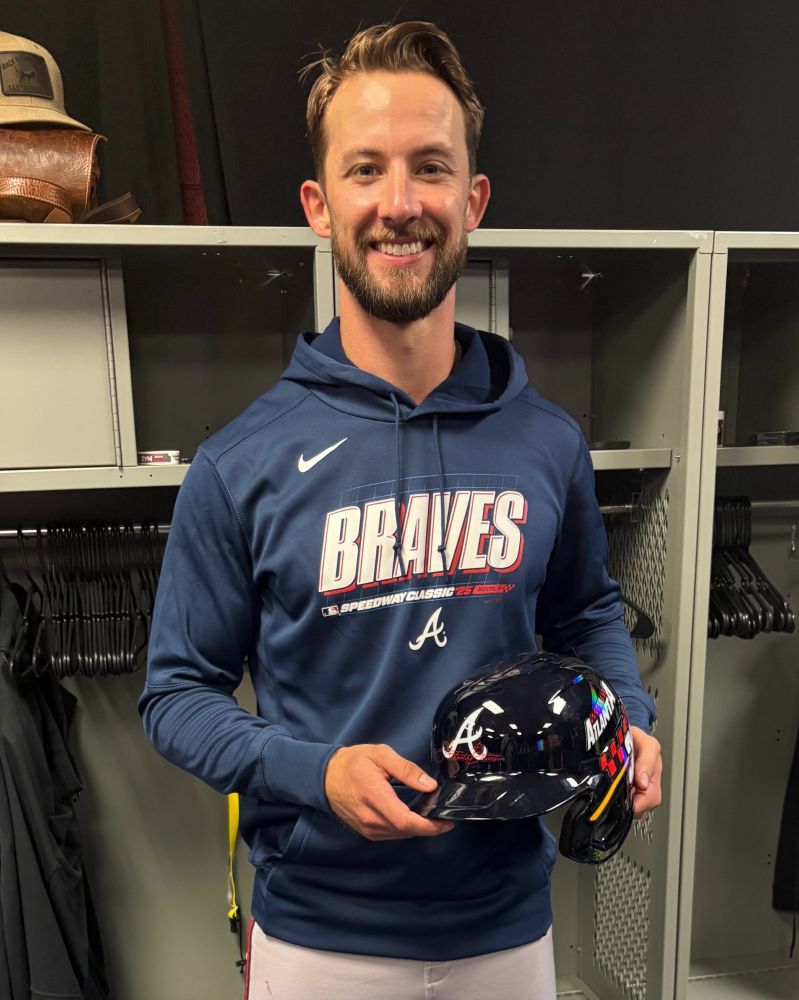 Eli White stands in the clubhouse holding a Braves helmet with a commemorative checkered pattern on the left side.