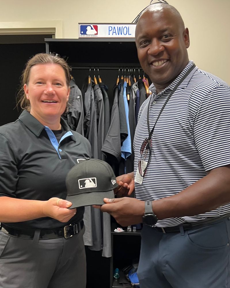 Jen Pawol and Michael Hill hold the black MLB cap worn by Pawol on August 9, 2025, when she became the first woman to umpire in a regular-season major league game.