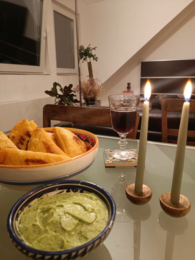 An image shows a plate with empanadas en avocado sauce with two lit candles and a cup of wine.
