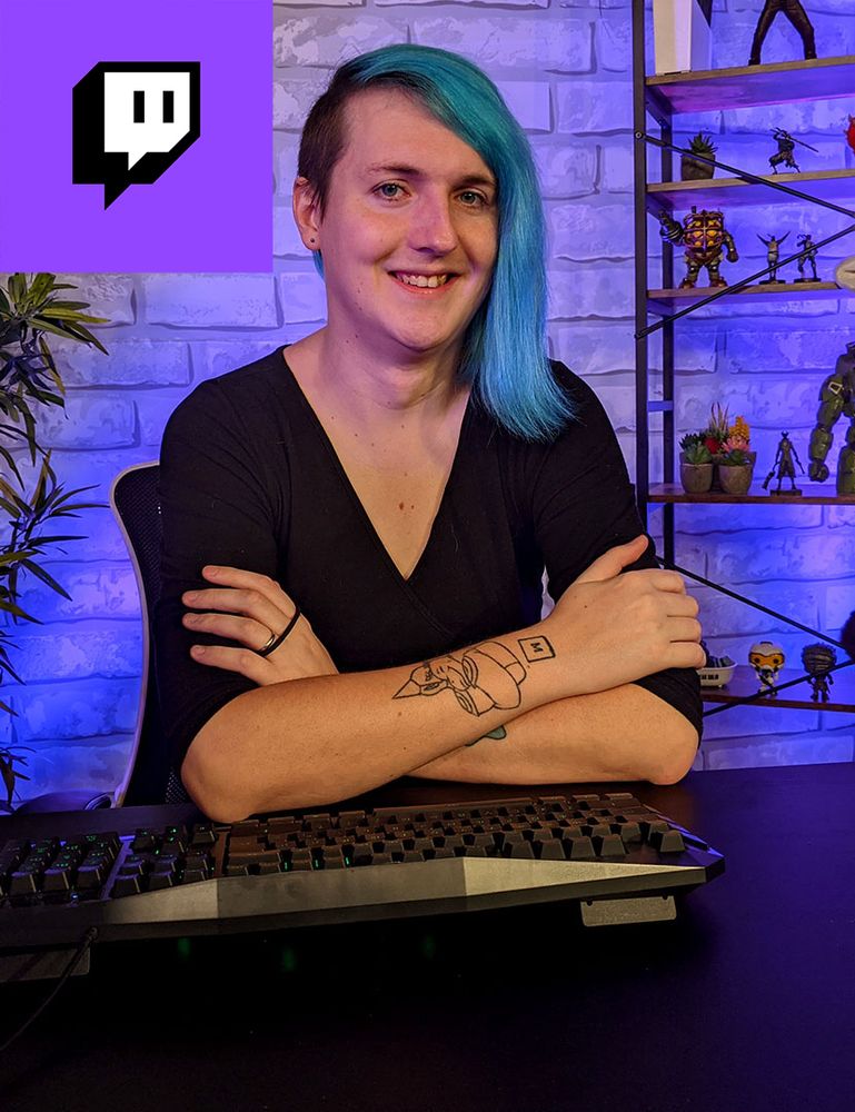 Laura is sat at a desk, with a keyboard in front of her and a shelf of gaming toys behind her. The Twitch logo is in the top left corner.