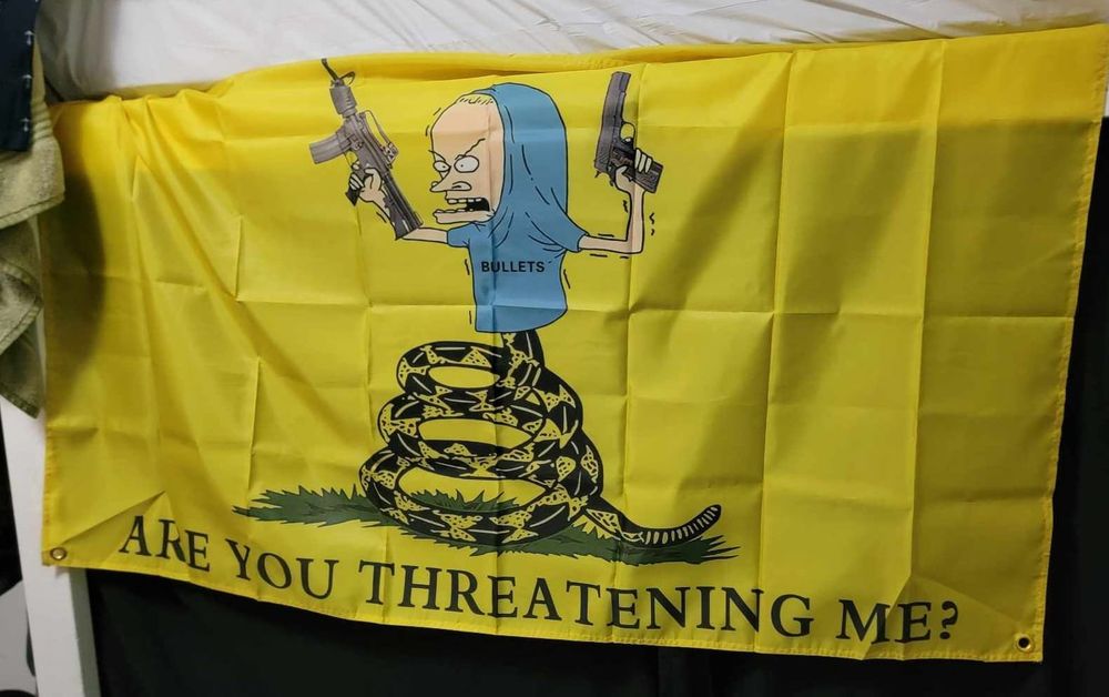 A "don't tread on me" flag with the head of the snake replaced by Beavis doing Cornholio with a gun in each hand. In the place of the usual slogan, it says, "are you threatening me?"