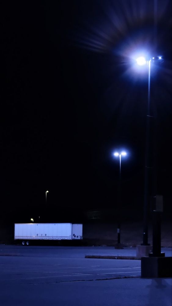 An empty late night parking lor, lit by defective LED lights that glow purple. 