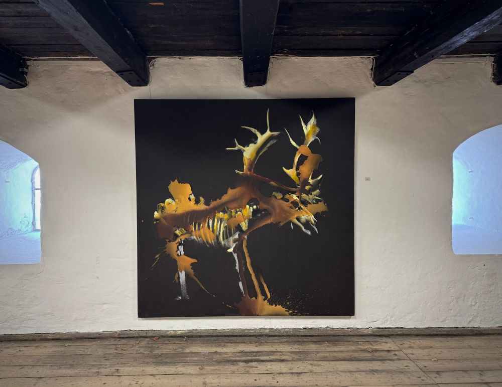 A painting about two meters by two meters, under visible timbered ceiling against white walls with two deep window alcoves, a meter or so deep. The painting has a black background and is of a game animal, maybe a reindeer? But kind of a skeleton of the animal, its face is like a skull. There are brishes of browns and dark oranges that dont seem directly representational but are somehow very horror esque.