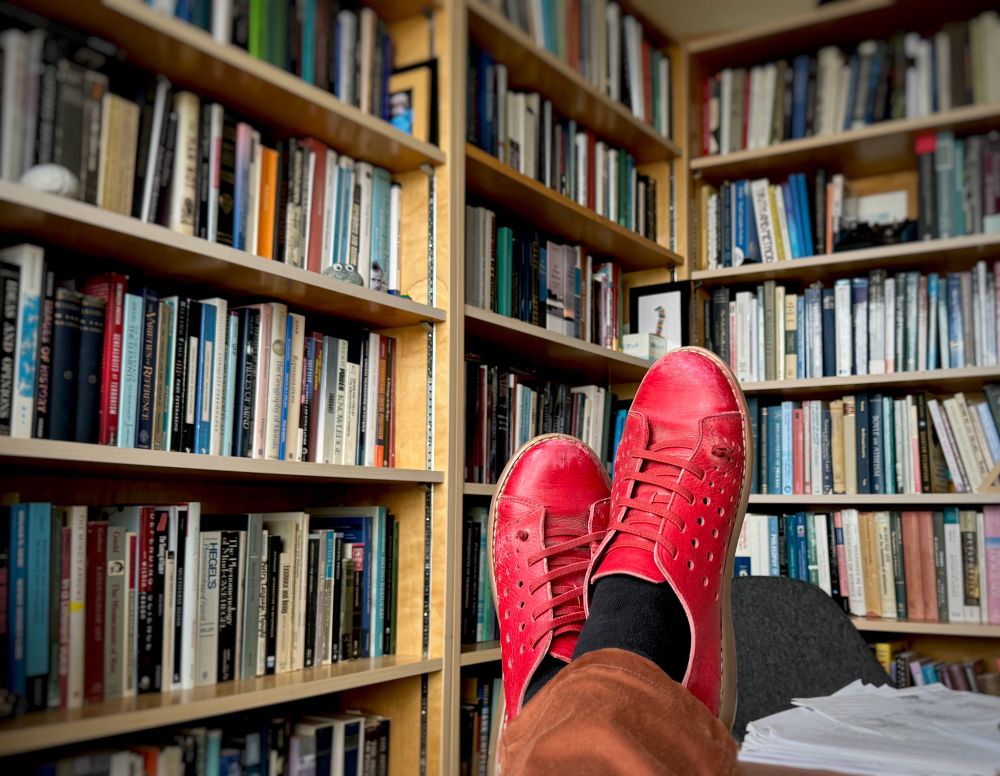 A pair of bright red shoes on the authors feet in a book filled office