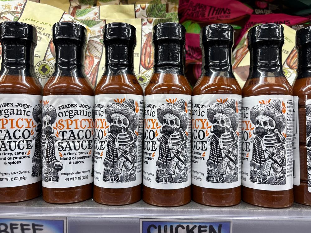 A shelf of Trader Joe’s taco sauce; the labels have drawings of skeletons wearing sombreros.