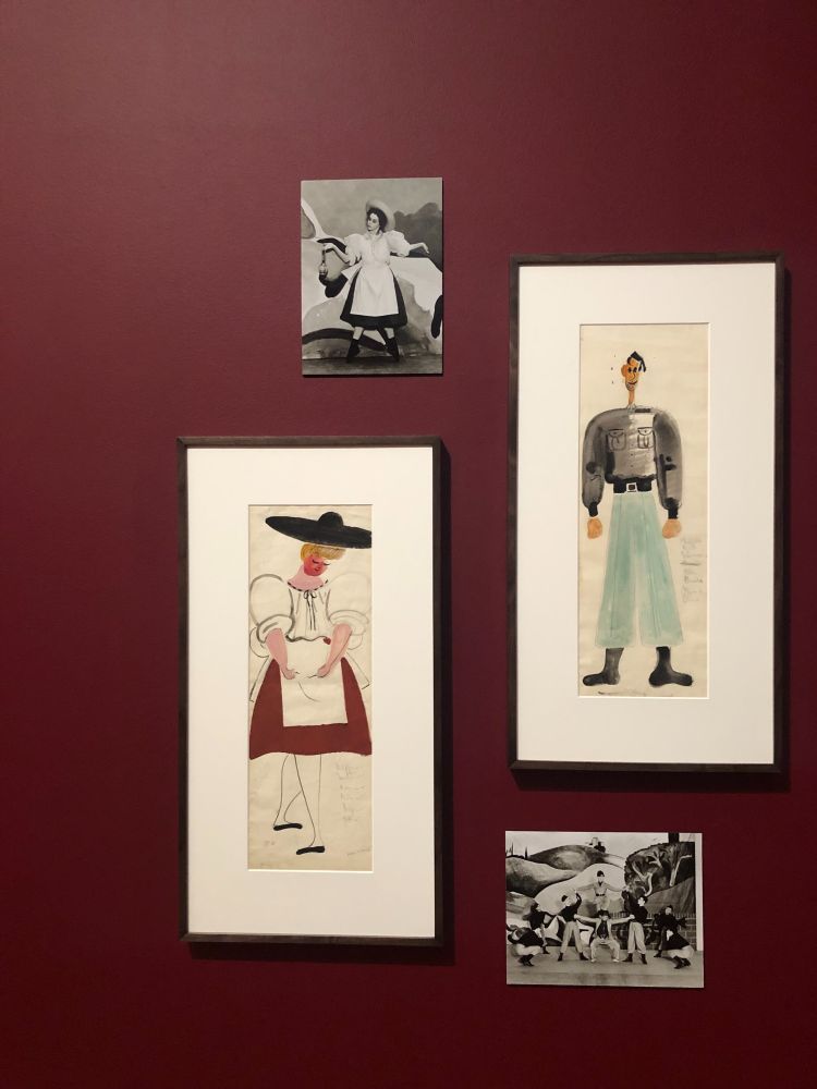 a maroon coloured gallery wall showing a selection of costume designs and black and white photos of dancers wearing them