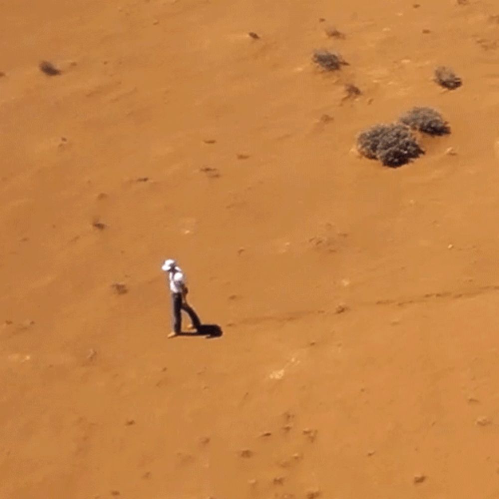 a man in a white shirt is walking through a sandy desert