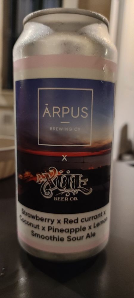 A beer can on top of a table. The brand is Ārpus in collaboration with Xul Beer Co. The flavor is Strawberry x Red currant x Coconut x Pineapple x Lemon Smoothie Sour Ale.