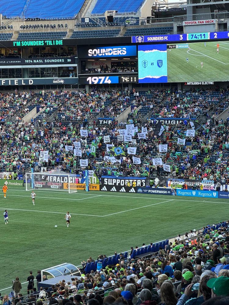 The supporters section at the Sounders match hold signs saying “chinga la migra”