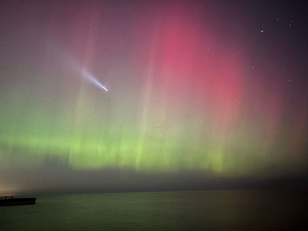 Northern lights glowing red and green over Lake Michigan with a plane flying through 