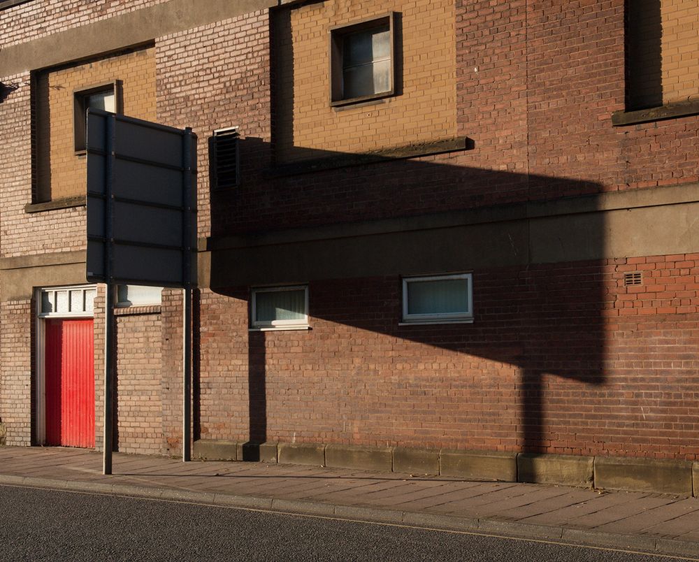 Low evening sun casting a long shadow from a road sign along a brick building.
