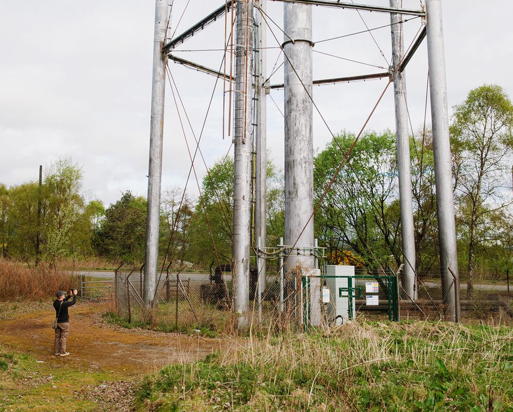 Photographer composing a photograph of a metal water tower, with just the legs of the structure in frame.