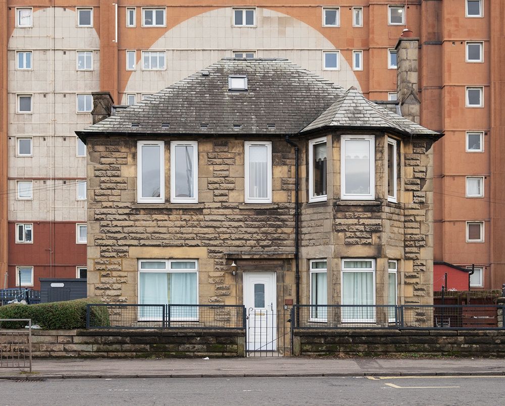 Colour photograph of a detached stone village in front of a much larger block of flats.