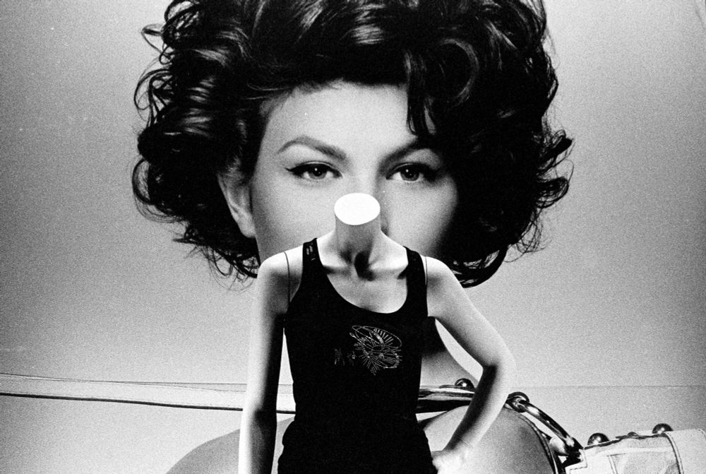 A mannequin in front of a large portrait of a woman with curly hair. In black and white. 