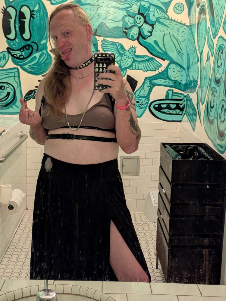 An outfit selfie of a trans woman in a public bathroom mirror