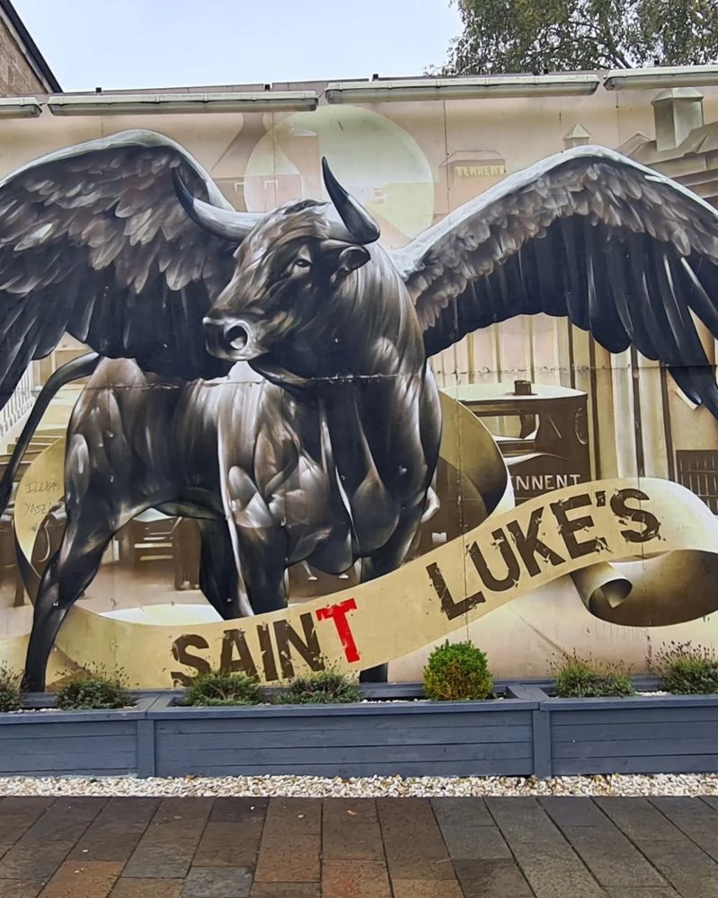 Street art of St. Luke's building. It shows a  bull having wings on their backs. A banner is at bottom, it says "St Luke's"