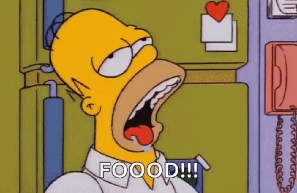 homer simpson is sitting in front of a refrigerator with his mouth open and his tongue out .