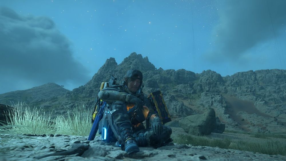 Death Stranding 2: Sam is sitting down in front of a mountainous landscape
