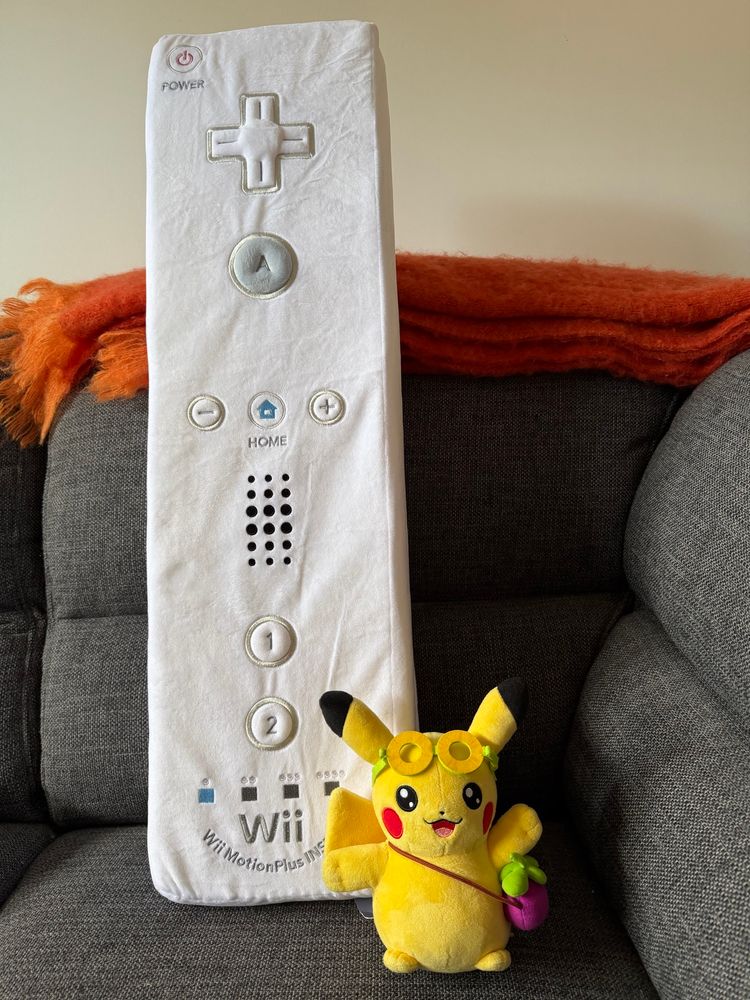A jumbo-sized Wii Remote pillow laid behind a Taipei Pikachu 