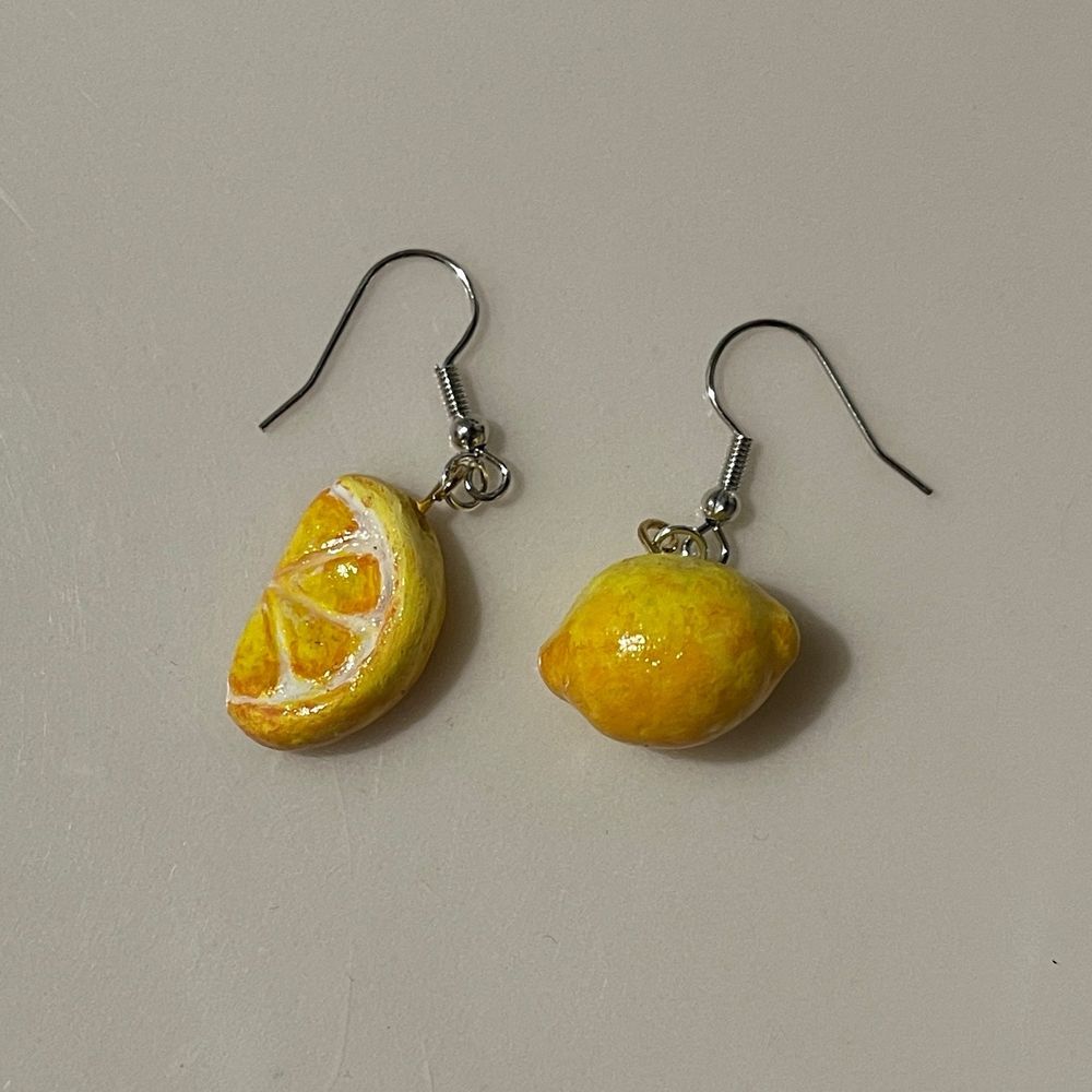 A photo of a polymer clay earring set; on the left is a lemon wedge, and on the right is a full lemon