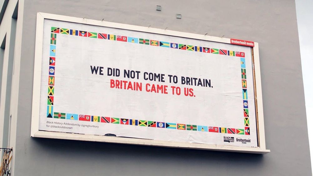 A white billboard with a border of flags of countries that were colonised by Britain. The text on the billboard reads "we did not come to Britain, Britain came to us" 